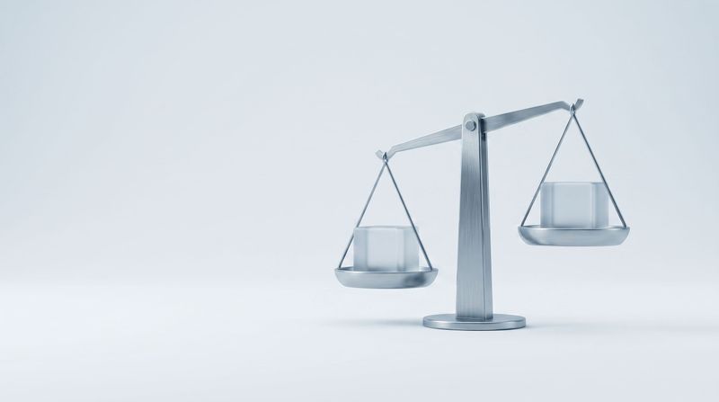 A steel balance scale holding a frosted glass cube on each pan